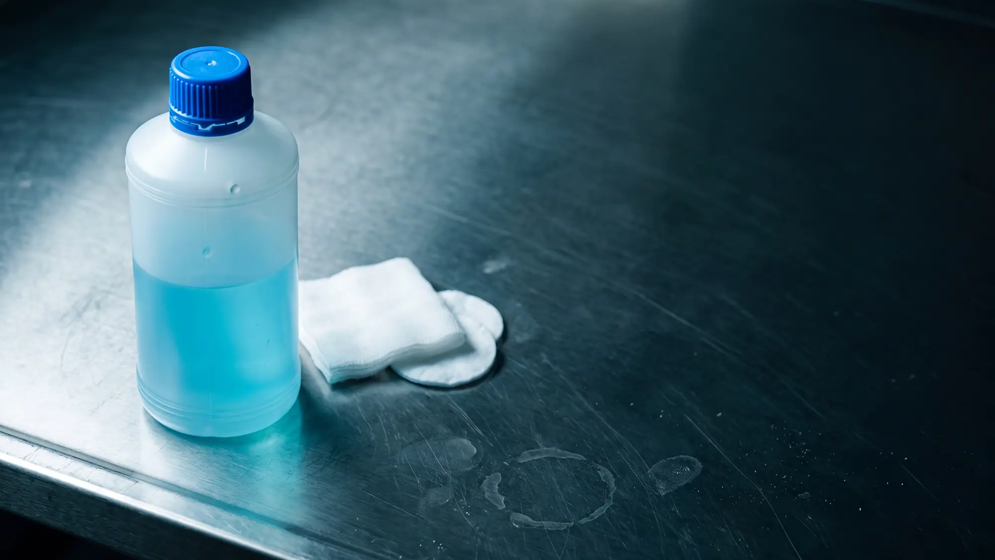Botella de alcohol antis&eacute;ptico junto a gasa sobre una mesa de acero